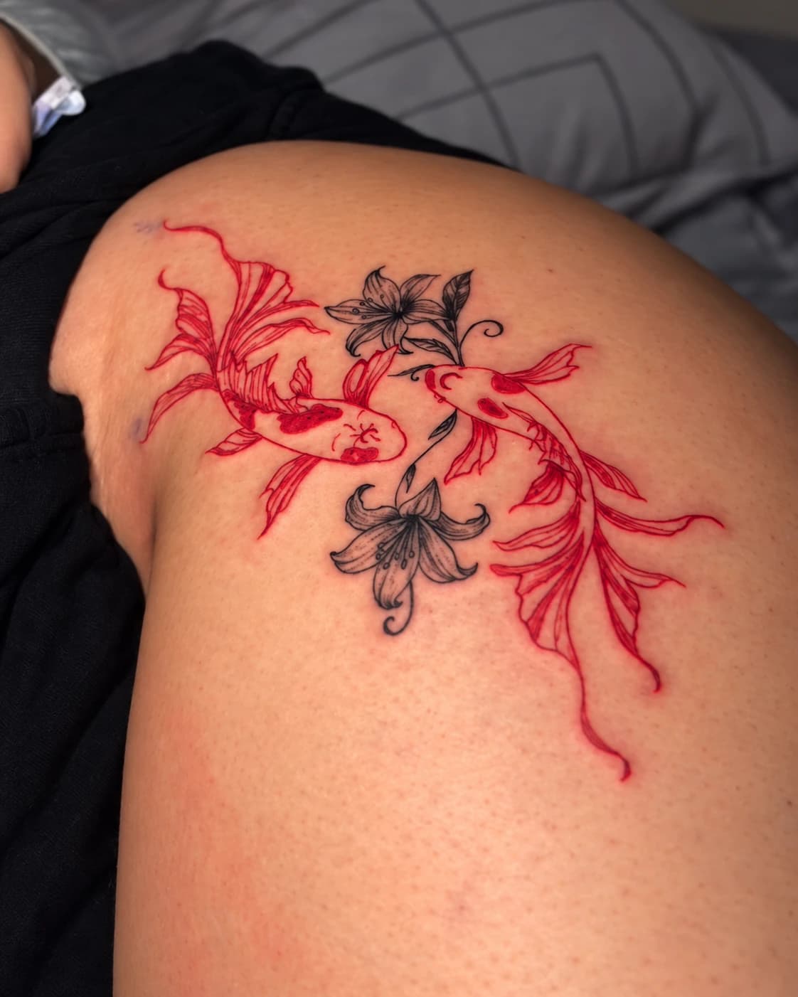 Two red koi fish with black flowers tattooed on a thigh