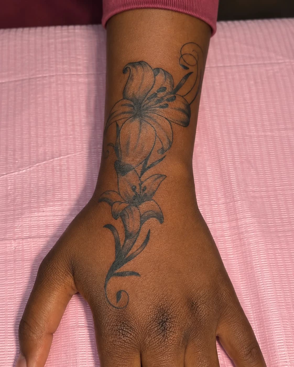 Black lily and flowing stems tattooed across the back of a hand