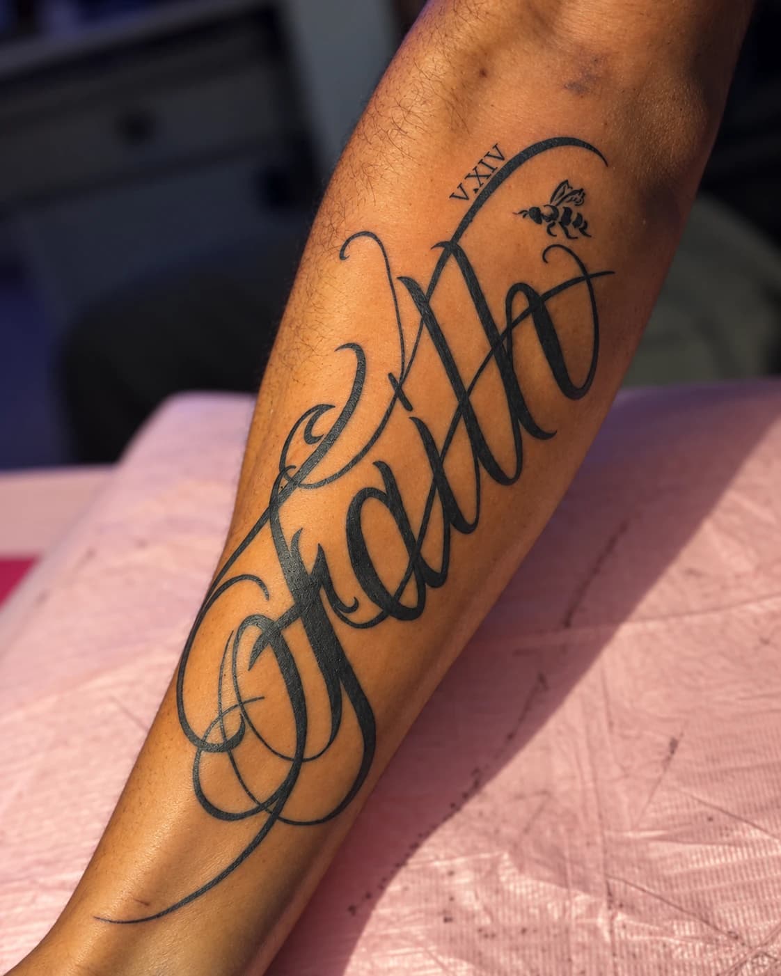 Flowing script tattoo with a small rose and Roman numerals on a forearm